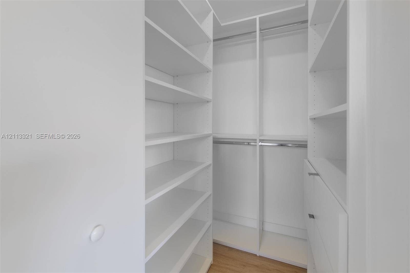 Walk-in closet featuring white built-in shelving, integrated hanging rods, soft-close drawer units, and wood-finish flooring