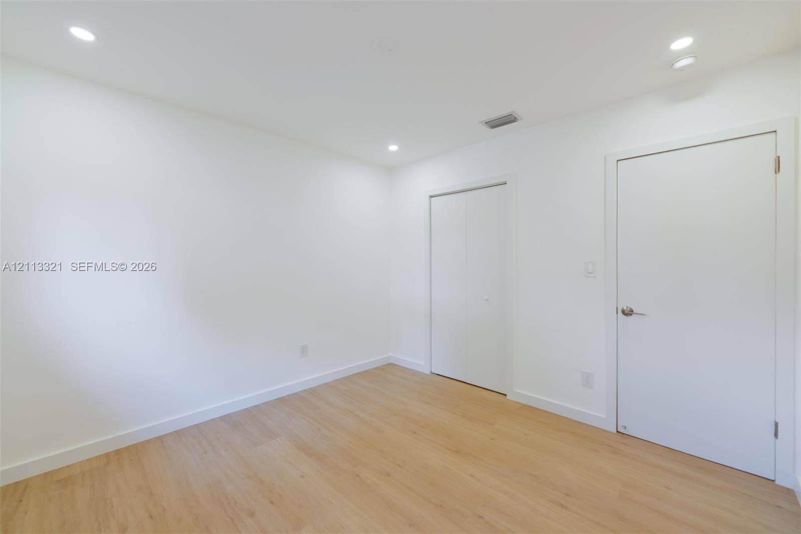 Interior space featuring wood-finish flooring, recessed lighting, and white walls, including a standard interior door and a double-panel closet door