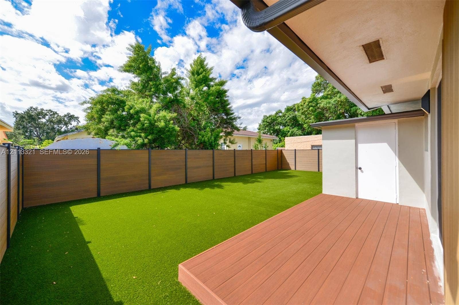 Backyard featuring a synthetic turf lawn, composite wood-finish decking, horizontal slat privacy fencing, and an exterior storage closet