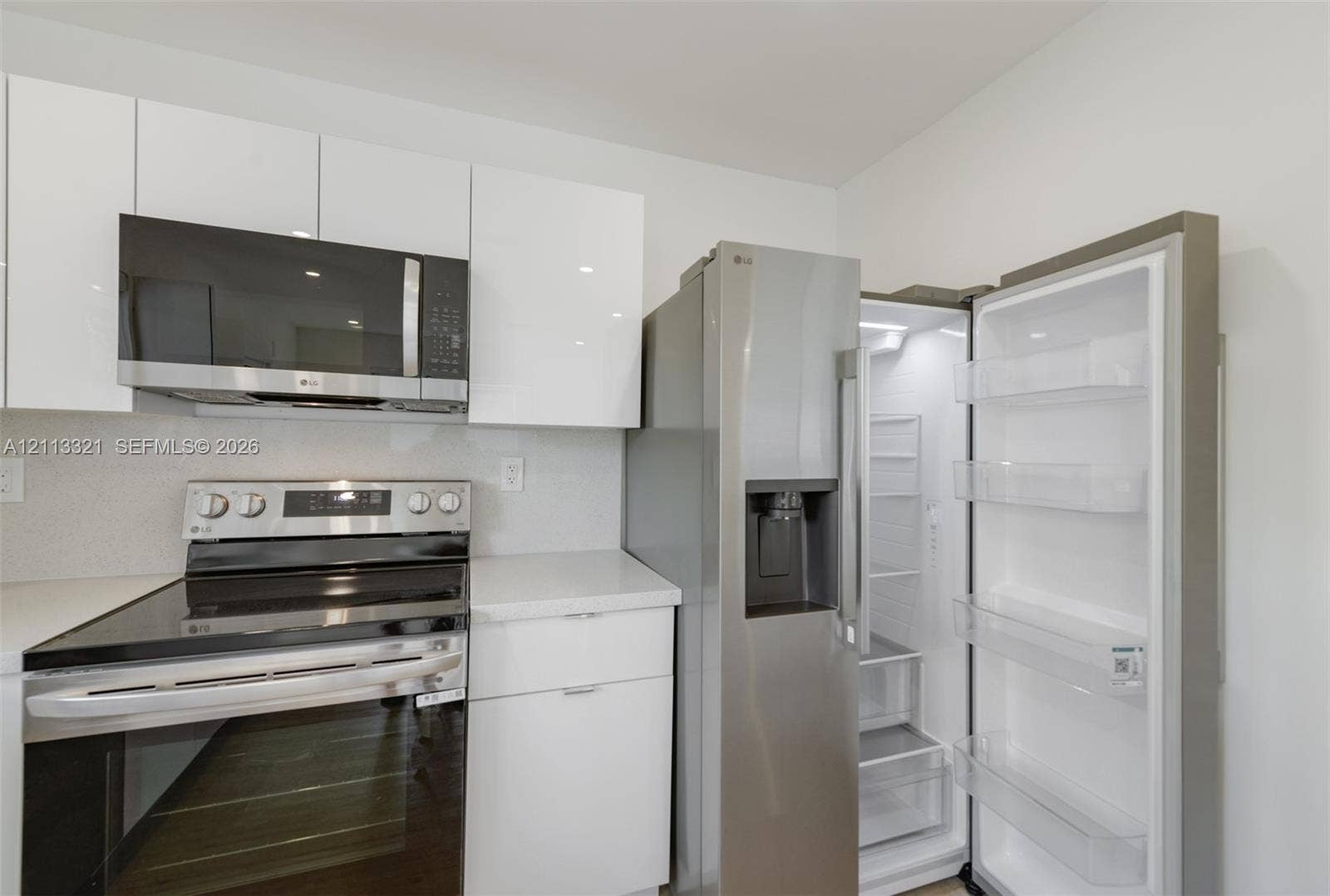 Kitchen featuring high-gloss white flat-panel cabinetry, stone-finish countertops, stainless steel microwave, stainless steel slide-in range, and stainless steel refrigerator with door-mounted ice and water dispenser