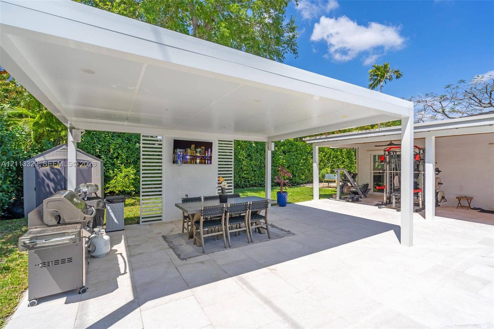 6440 SW 144th Street, Coral Gables, FL 33158 Covered outdoor patio featuring a flat-roof structure with recessed lighting, light-toned stone tile flooring, and vertical slatted privacy screening