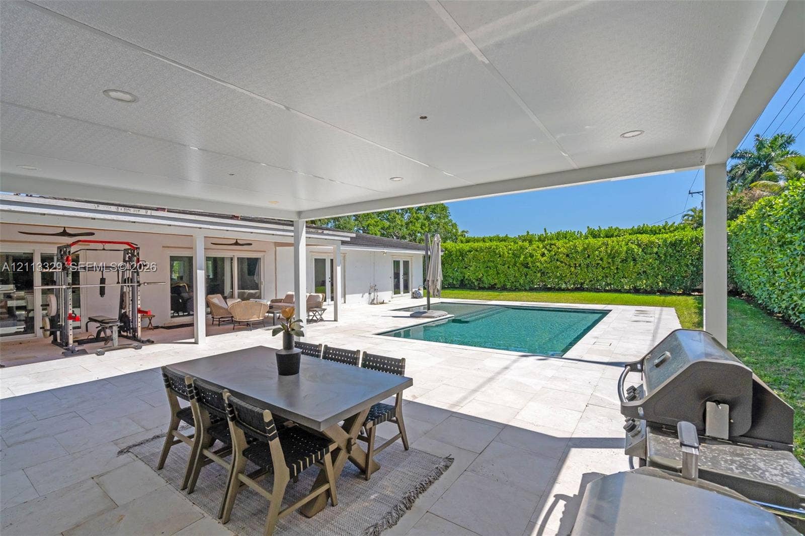 6440 SW 144th Street, Coral Gables, FL 33158 Covered patio featuring recessed lighting, light-toned stone flooring, an inground swimming pool, and a privacy hedge