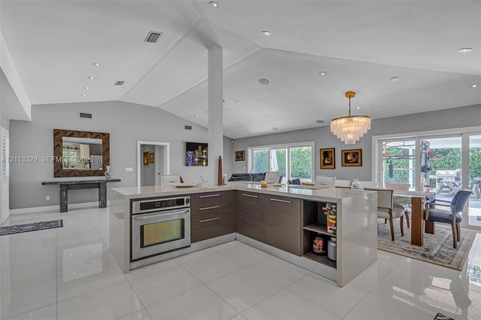 6440 SW 144th Street, Coral Gables, FL 33158 Open-concept interior featuring a vaulted ceiling, recessed lighting, polished large-format tile flooring, and a kitchen island with built-in oven and wood-finish cabinetry