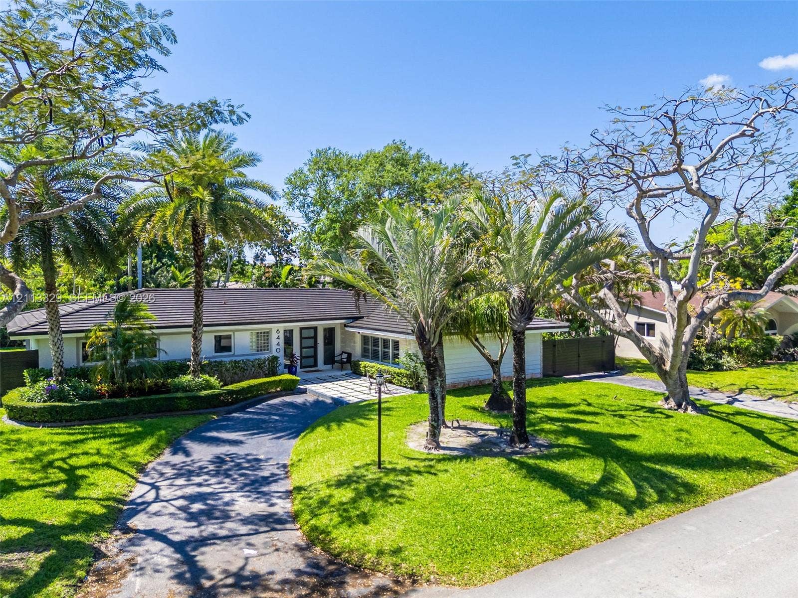 6440 SW 144th Street, Coral Gables, FL 33158 Single-story residence featuring a dark-tiled hip roof, paved circular driveway, manicured landscaping, and mature palm trees
