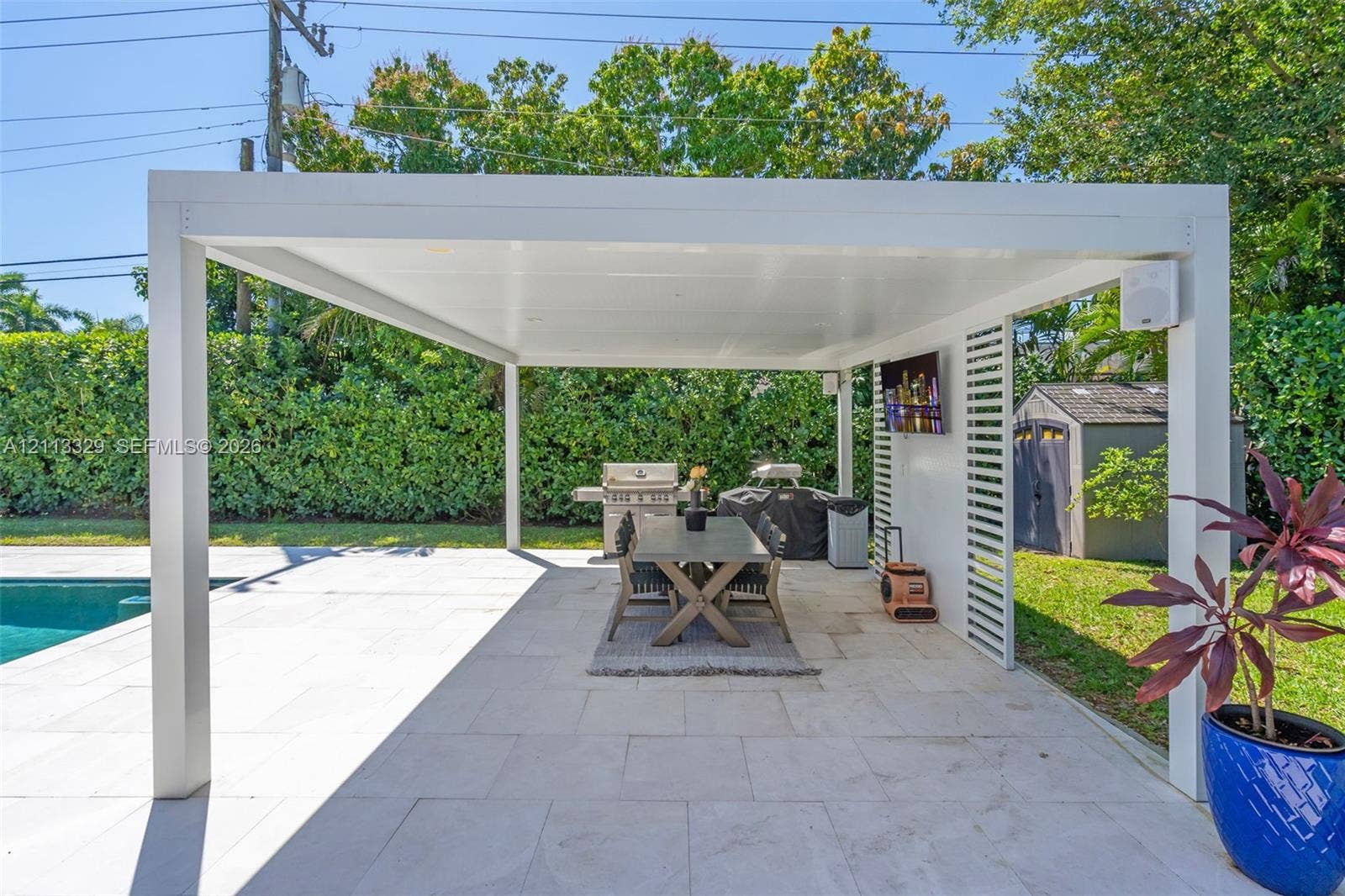 6440 SW 144th Street, Coral Gables, FL 33158 Covered outdoor living space featuring a white aluminum pergola, light-toned stone patio flooring, built-in recessed lighting, and a slatted privacy screen