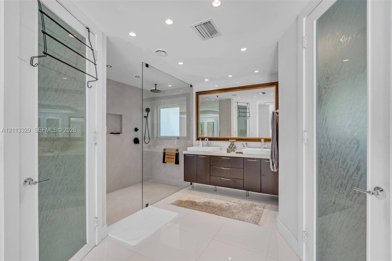6440 SW 144th Street, Coral Gables, FL 33158 Floating dark-wood cabinetry with dual rectangular vessel sinks, walk-in glass-enclosed shower featuring matte black fixtures, and large framed wall mirror
