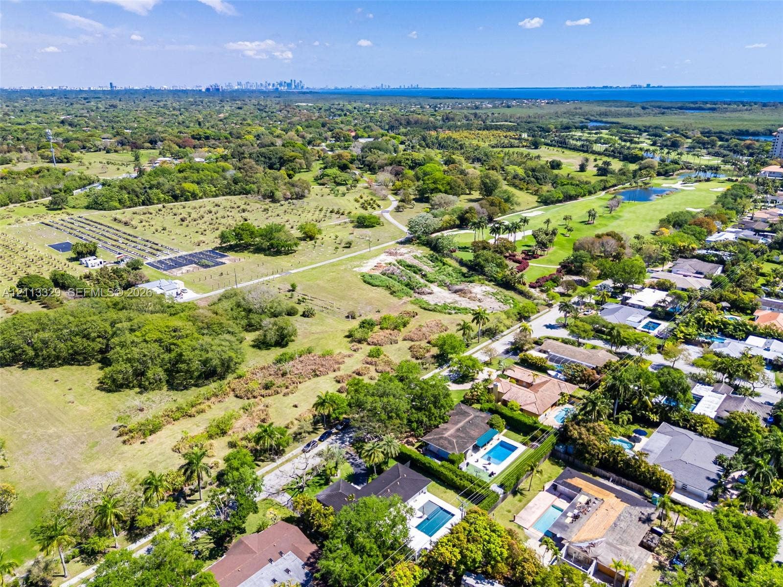 6440 SW 144th Street, Coral Gables, FL 33158 Aerial perspective of a residential neighborhood featuring expansive green space, mature canopy trees, water features, and a distant cityscape skyline