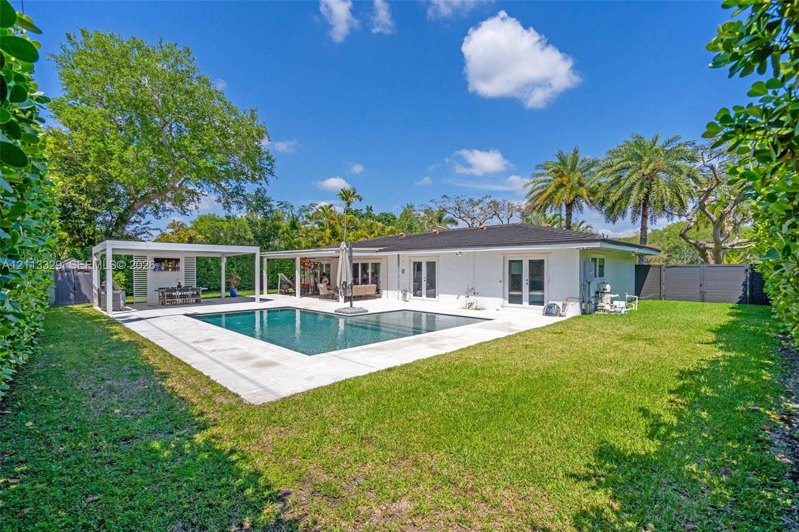 6440 SW 144th Street, Coral Gables, FL 33158 Backyard featuring a swimming pool, concrete patio, covered pergola, expansive lawn, and perimeter privacy hedges