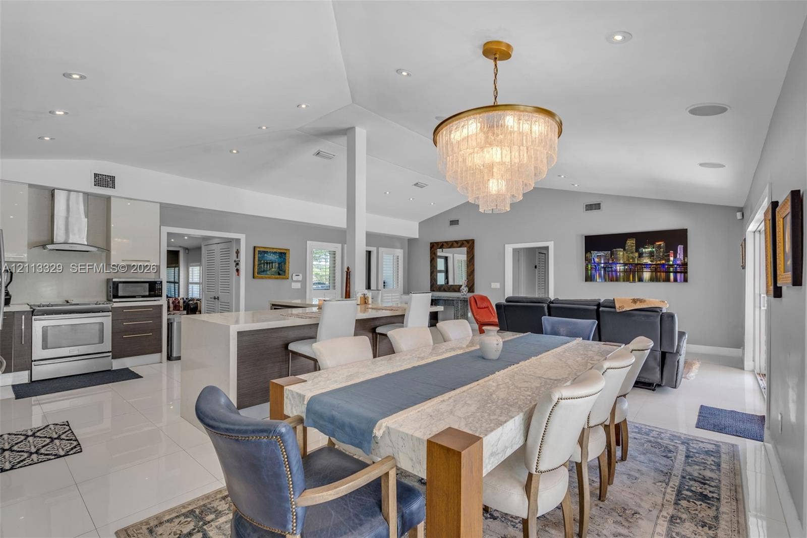 6440 SW 144th Street, Coral Gables, FL 33158 Vaulted ceilings with recessed lighting, large central kitchen island with waterfall countertop, high-gloss cabinetry, stainless steel range with overhead ventilation, and a tiered crystal chandelier