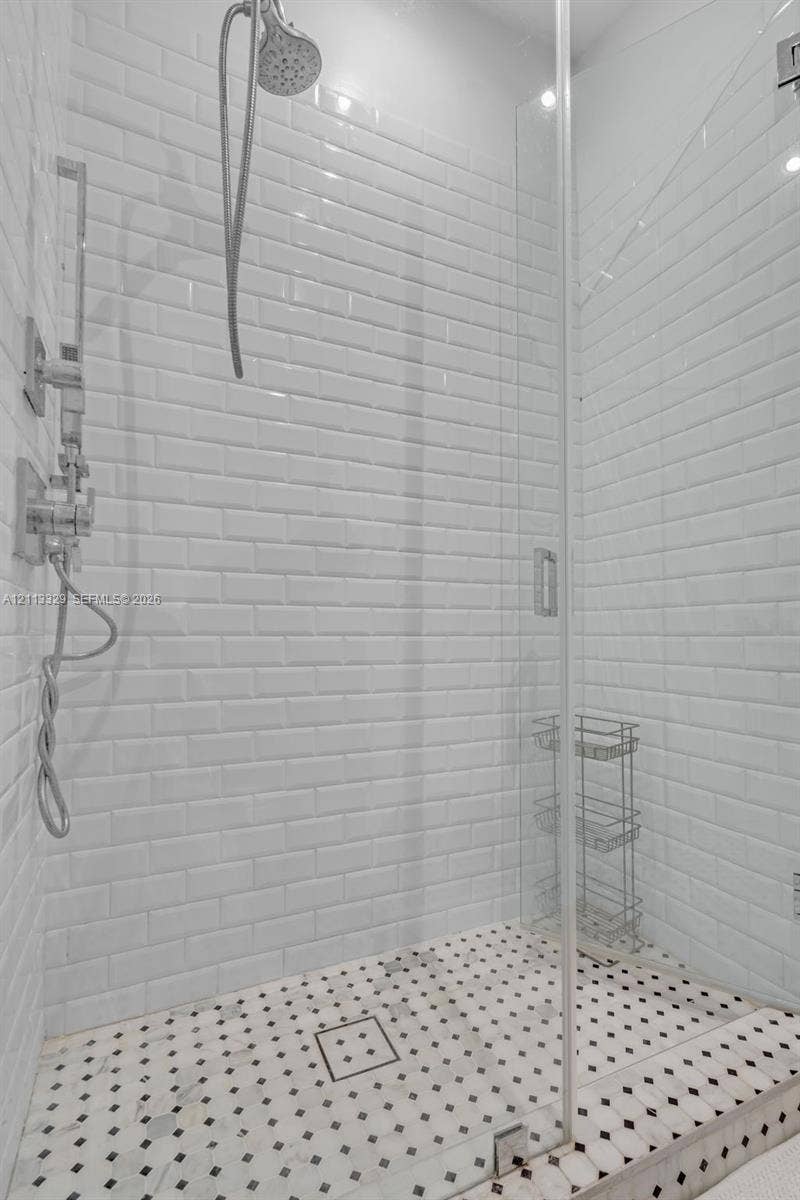 6440 SW 144th Street, Coral Gables, FL 33158 Walk-in shower featuring white subway tile walls, geometric patterned tile flooring, a frameless glass door, and polished chrome plumbing fixtures