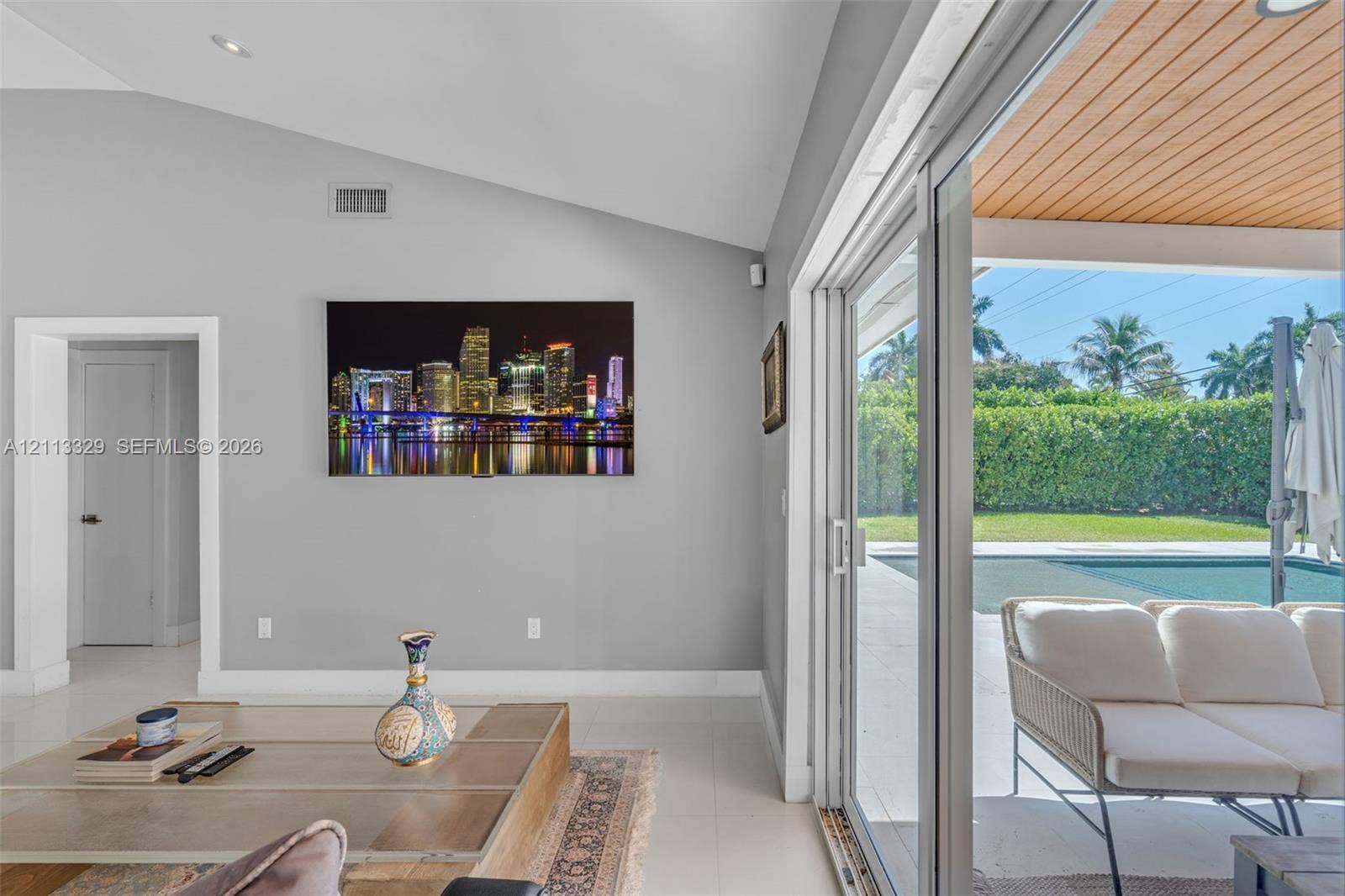 6440 SW 144th Street, Coral Gables, FL 33158 Vaulted ceilings, large-format tile flooring, and floor-to-ceiling sliding glass doors opening to a covered patio with wood-paneled ceiling, manicured landscaping, and a pool