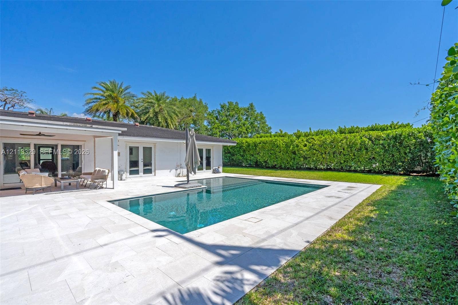 6440 SW 144th Street, Coral Gables, FL 33158 Rectangular swimming pool featuring a stone-paver deck, covered patio, and manicured perimeter landscaping