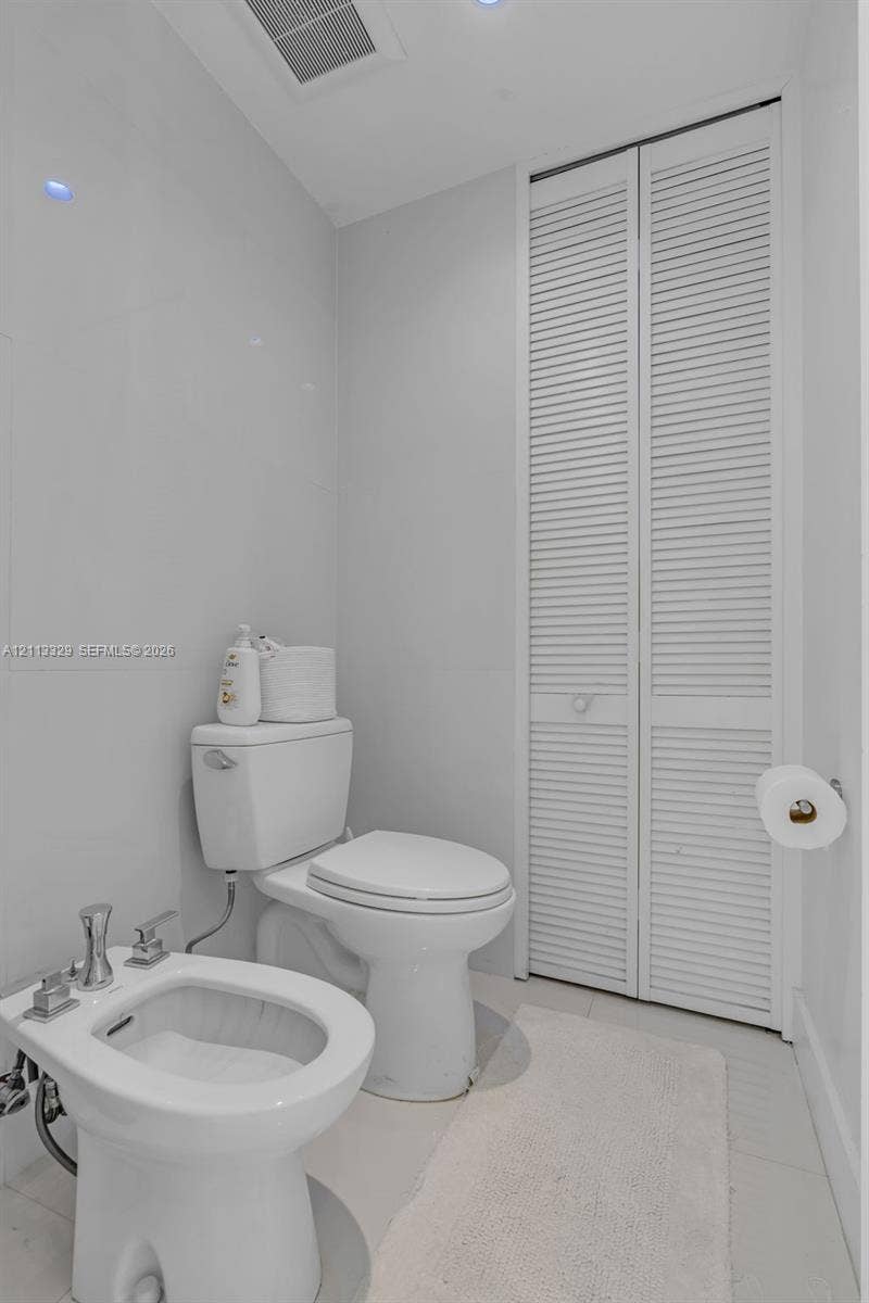 6440 SW 144th Street, Coral Gables, FL 33158 Restroom featuring a floor-mounted bidet with polished chrome fixtures, a standard-height toilet, and floor-to-ceiling louvered-style closet doors
