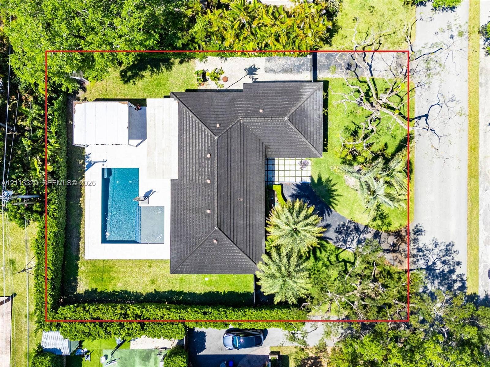 6440 SW 144th Street, Coral Gables, FL 33158 Aerial perspective of a property featuring a tiled hip roof, rectangular swimming pool, concrete patio, asphalt driveway, and mature landscaping