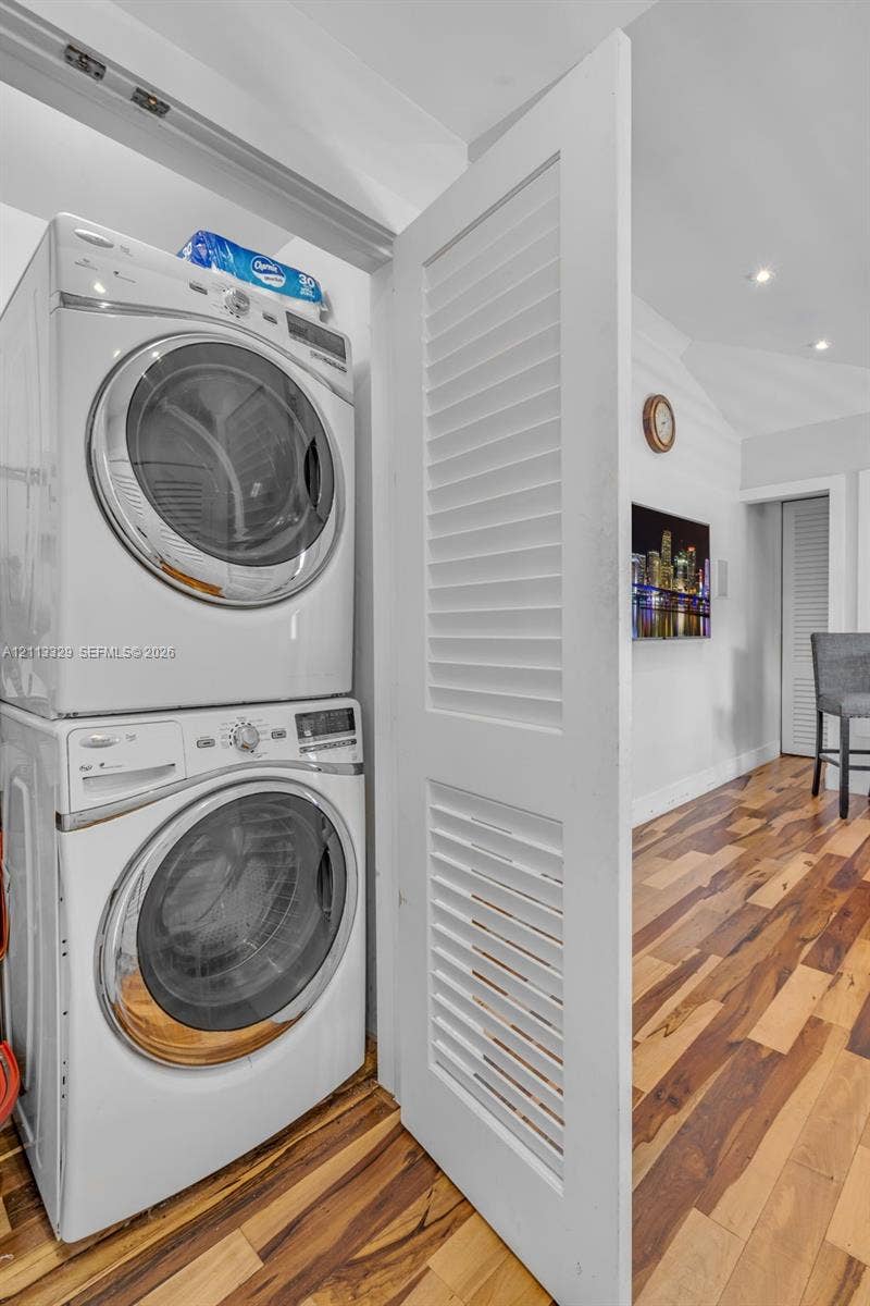 6440 SW 144th Street, Coral Gables, FL 33158 Stacked laundry unit concealed by a white louvered door, complemented by wood-finish flooring and recessed ceiling lighting