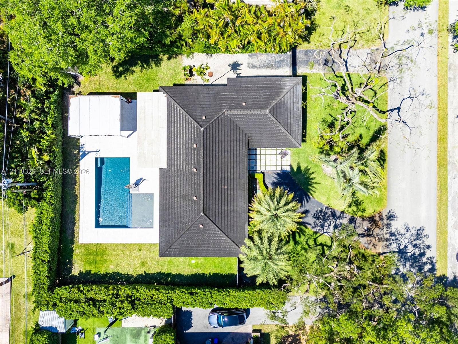 6440 SW 144th Street, Coral Gables, FL 33158 Aerial perspective of a property featuring a dark-tiled roof, a rectangular swimming pool, concrete patio space, and mature landscaping