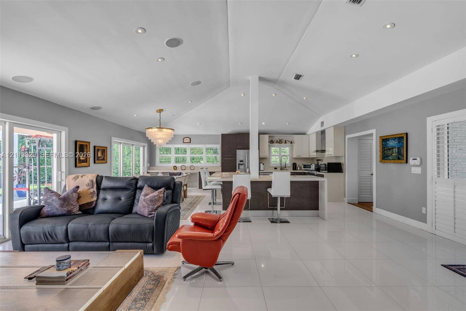 6440 SW 144th Street, Coral Gables, FL 33158 Open-concept interior featuring vaulted ceilings with recessed lighting, high-gloss tile flooring, a tiered kitchen island with quartz countertops, and a tiered crystal chandelier