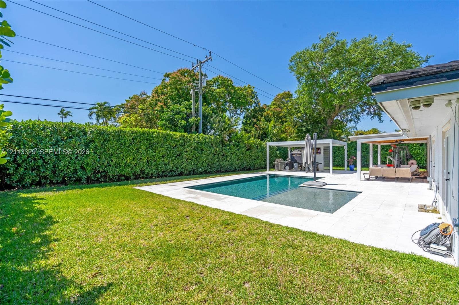 6440 SW 144th Street, Coral Gables, FL 33158 Backyard featuring an inground swimming pool, light-colored stone patio, covered pergola, and privacy hedges