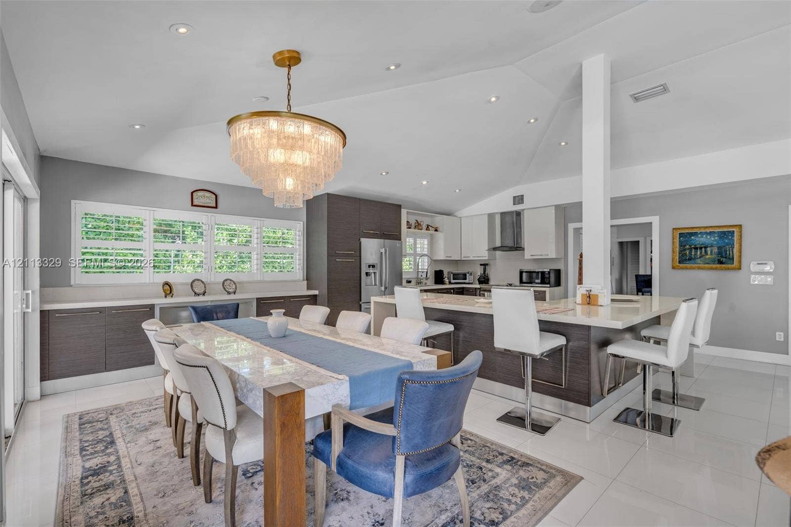 6440 SW 144th Street, Coral Gables, FL 33158 Open-concept kitchen and dining area featuring a vaulted ceiling, recessed lighting, multi-tone custom cabinetry, a stone-surfaced kitchen island, and polished tile flooring
