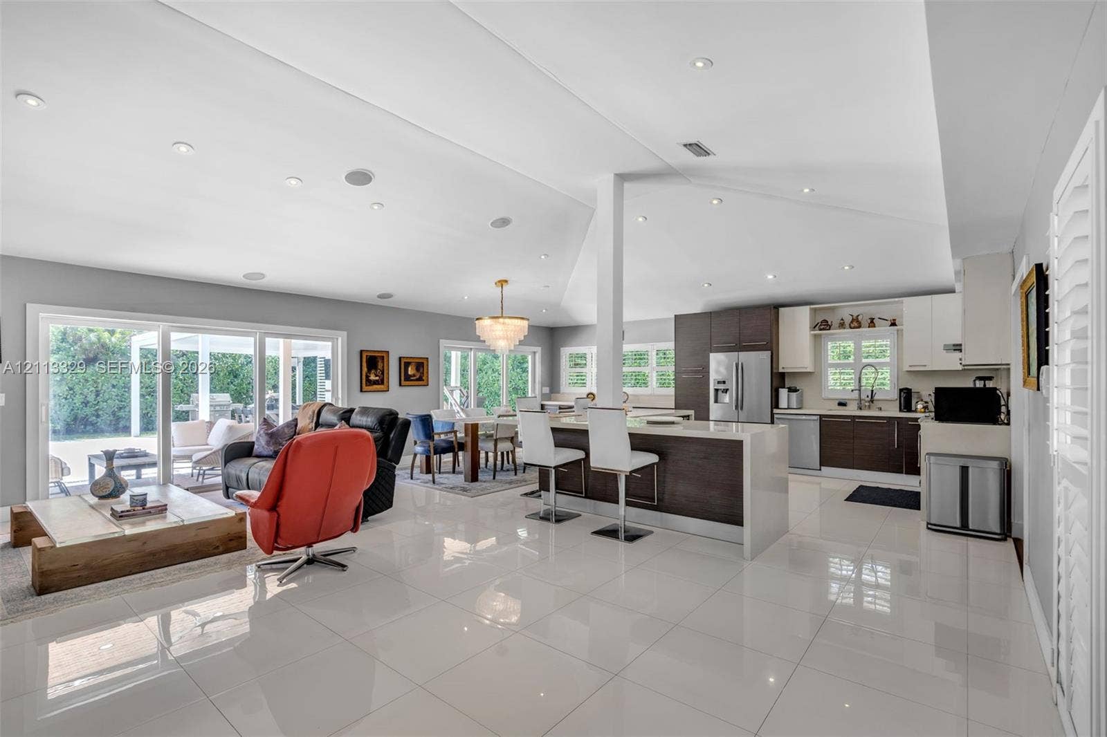 6440 SW 144th Street, Coral Gables, FL 33158 Open-concept interior featuring large-format tile flooring, vaulted ceilings with recessed lighting, kitchen island with quartz-style countertop, and dual sliding glass doors