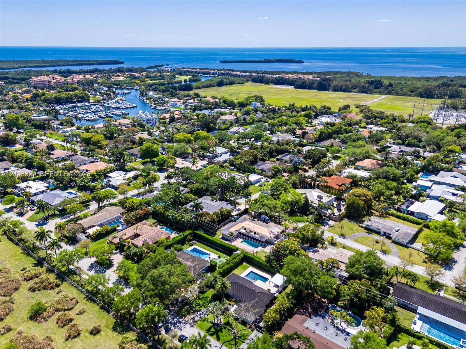 6440 SW 144th Street, Coral Gables, FL 33158 Aerial perspective of a coastal residential neighborhood featuring extensive tree canopy, manicured lawns, private swimming pools, and proximity to a marina and open water