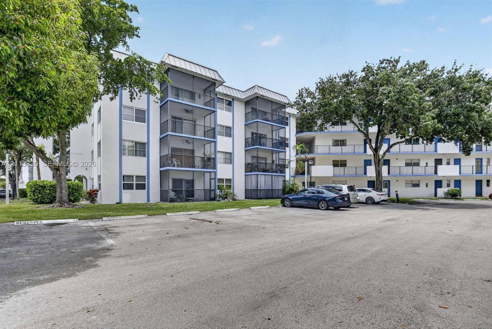6001 N Falls Cir Drive, #105, Lauderhill, FL 33319 Multi-story building exterior featuring screened-in balconies, metal roof accents, and mature landscaping