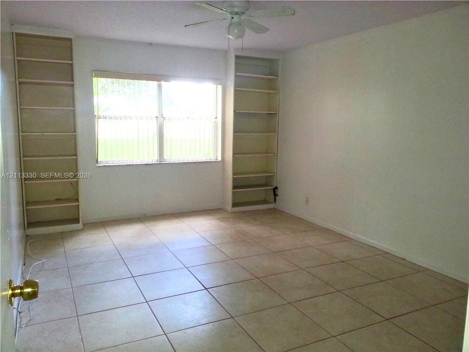 6001 N Falls Cir Drive, #105, Lauderhill, FL 33319 Room featuring neutral tile flooring, dual floor-to-ceiling built-in shelving units, and a ceiling fan