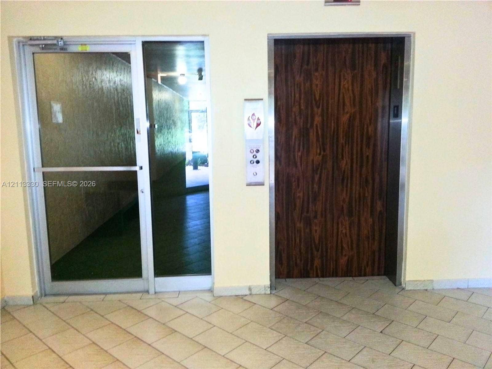 6001 N Falls Cir Drive, #105, Lauderhill, FL 33319 Commercial elevator featuring wood-finish paneling, metal frame, and vertical control panel, accompanied by a glass door with a metal frame