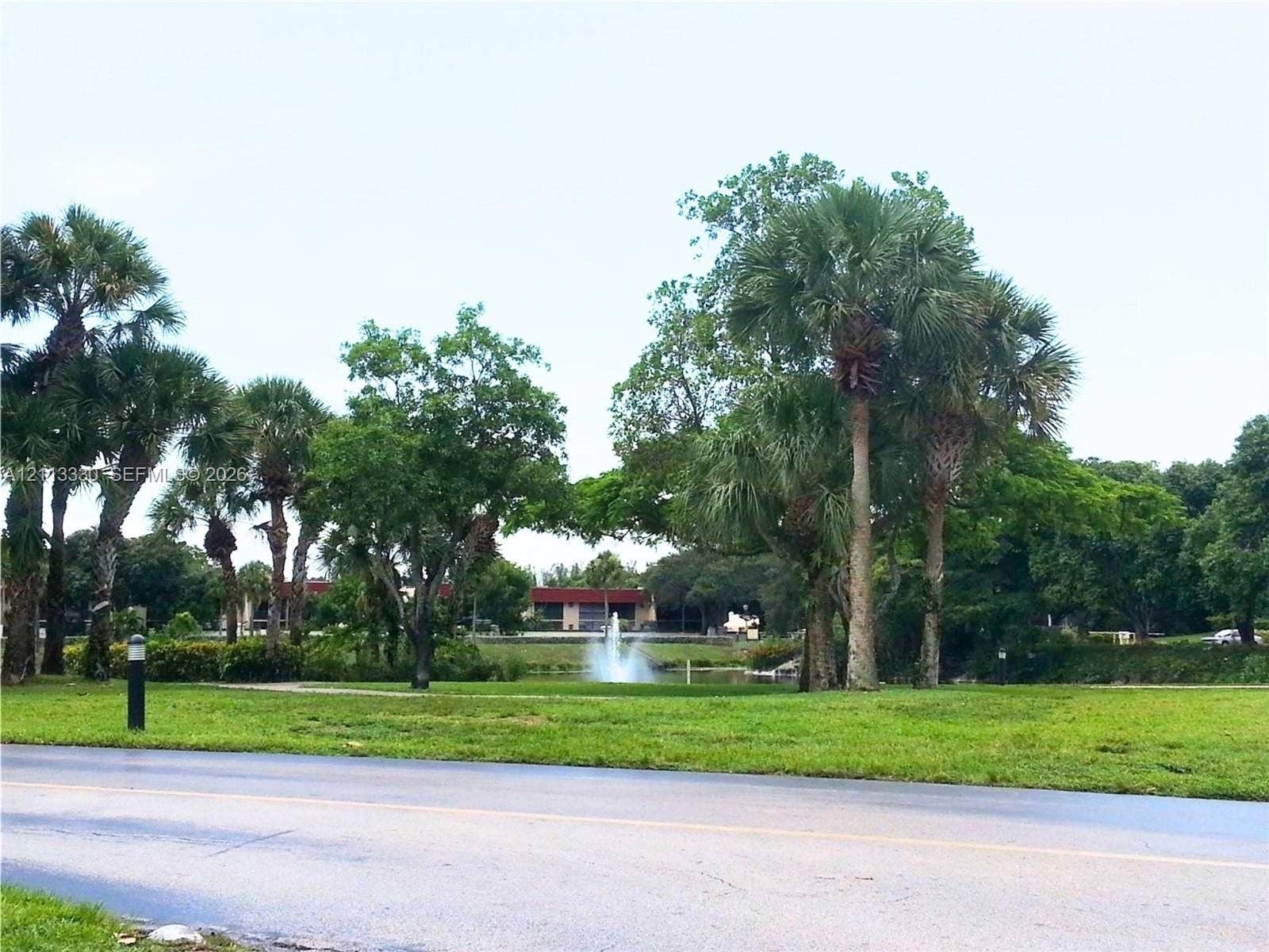 6001 N Falls Cir Drive, #105, Lauderhill, FL 33319 Grounds featuring mature palm trees, sprawling lawn, pond with fountain, and paved path