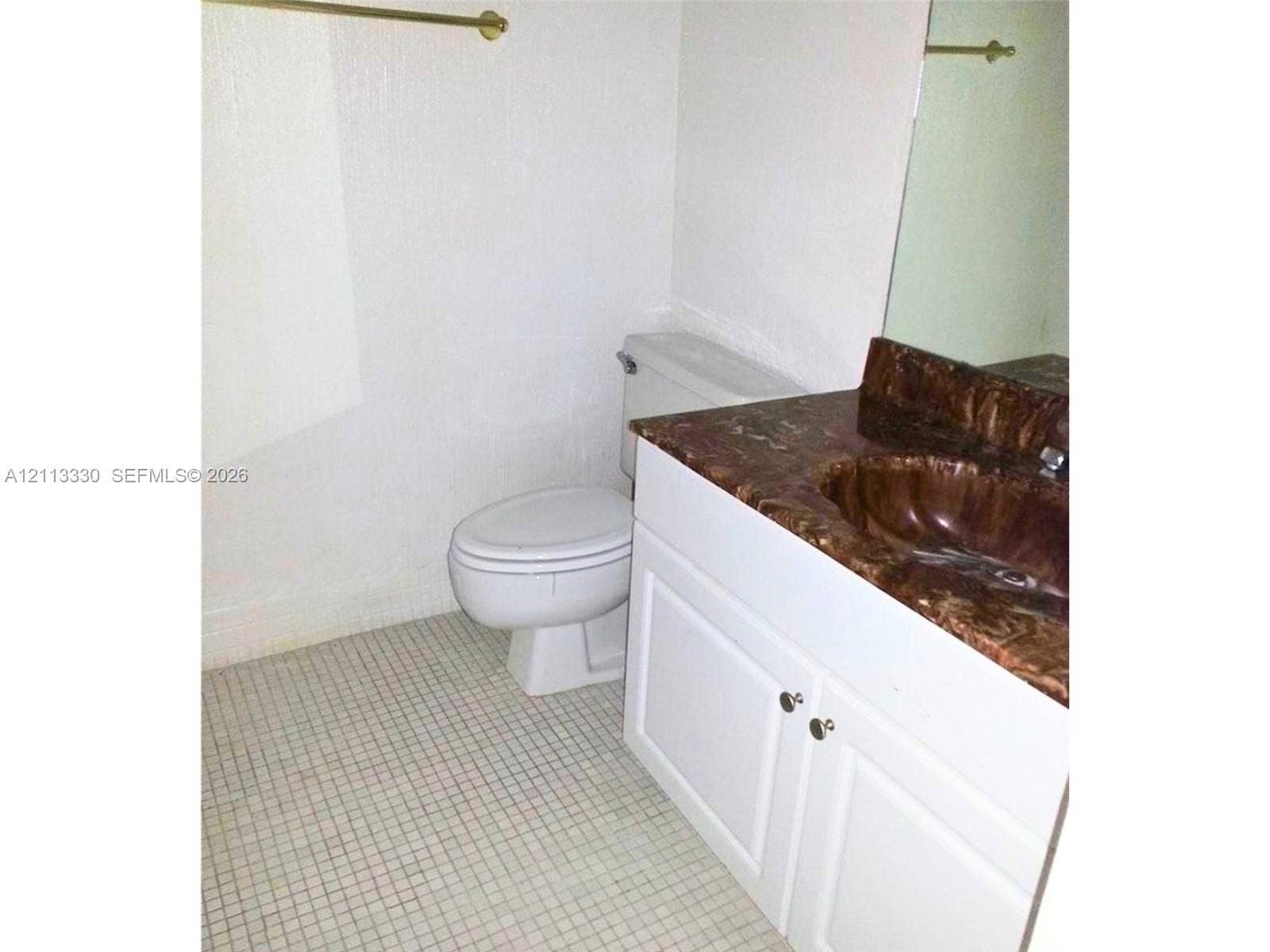 6001 N Falls Cir Drive, #105, Lauderhill, FL 33319 White vanity cabinet with a stone-finish countertop and integrated sink, paired with small-format tile flooring and a wall-mounted mirror