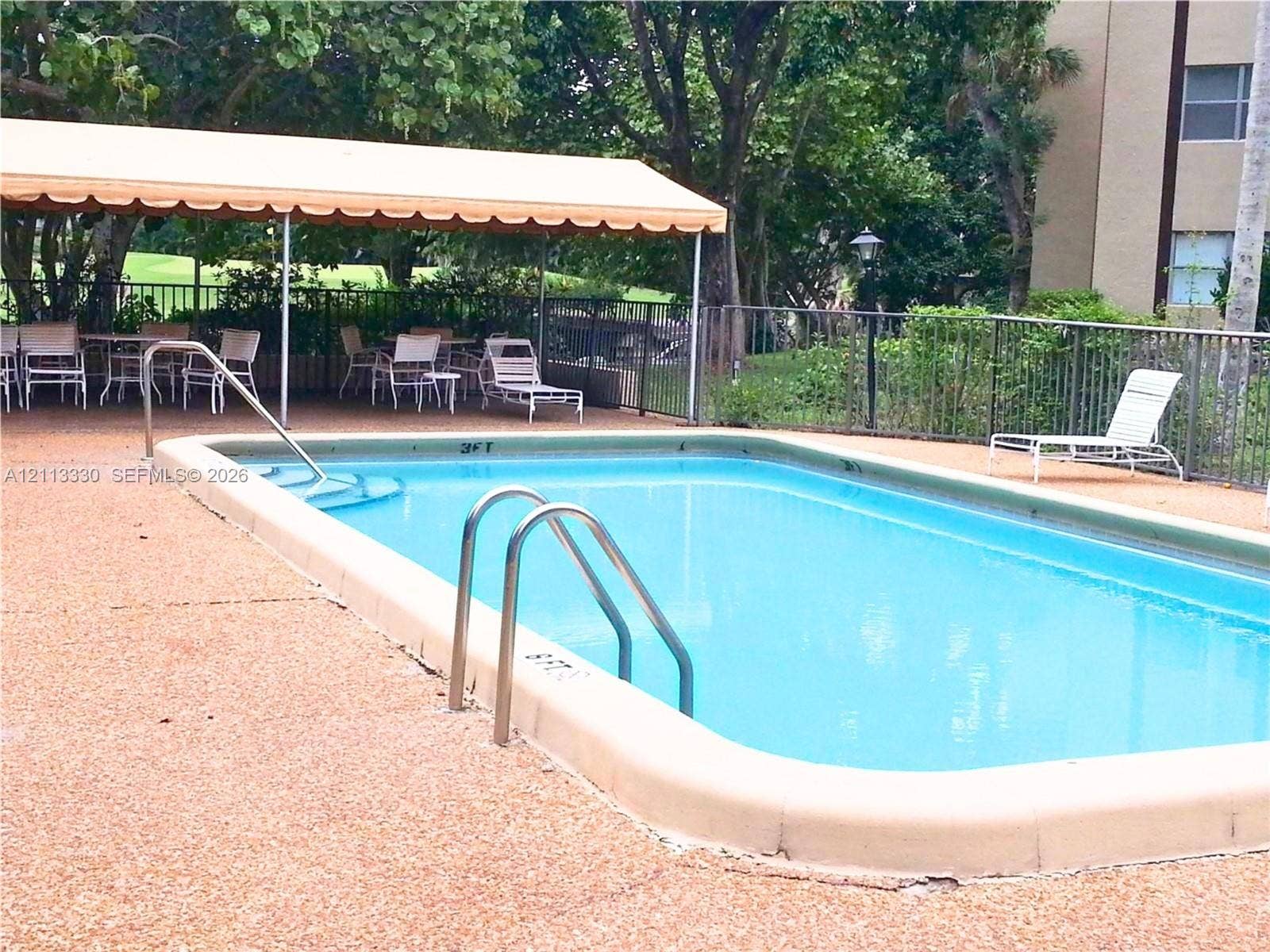6001 N Falls Cir Drive, #105, Lauderhill, FL 33319 Inground swimming pool with metal ladder and integrated steps, concrete deck, and overhead canopy
