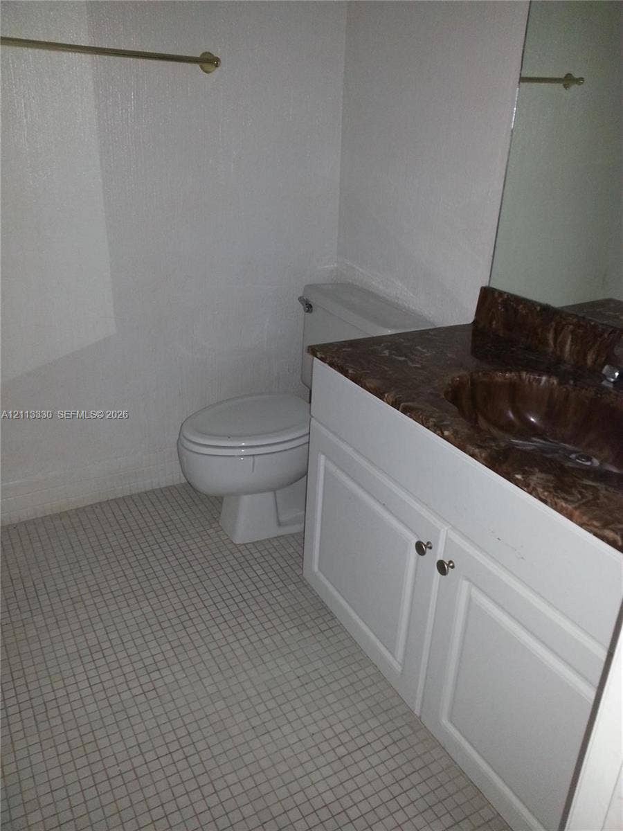 6001 N Falls Cir Drive, #105, Lauderhill, FL 33319 Vanity featuring a stone-look countertop with an integrated basin, white shaker-style cabinetry, a large wall-mounted mirror, and tile flooring