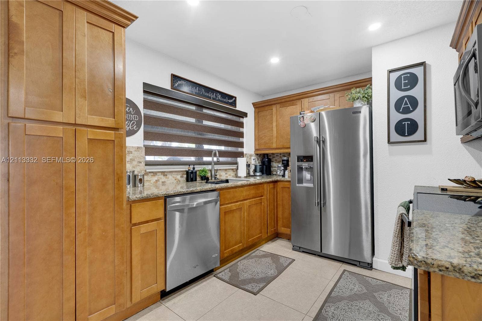 13111 SW 84th Street, Miami, FL 33183 Kitchen featuring medium-toned wood cabinetry, stone countertops, tiled backsplash, stainless steel appliances, and large-format floor tile