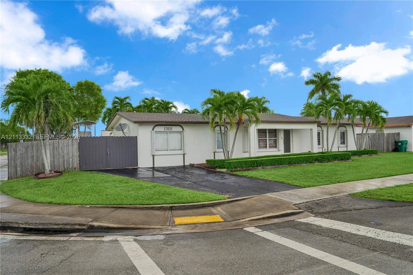 13111 SW 84th Street, Miami, FL 33183 Single-story exterior featuring a light-toned stucco facade, paved driveway, mature palm trees, and perimeter privacy fencing