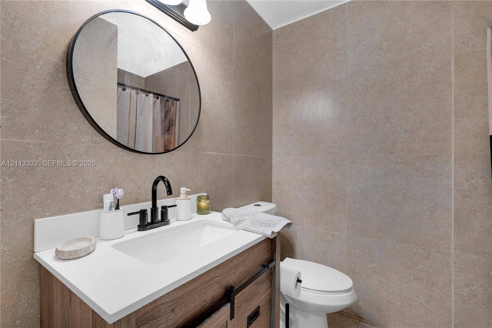 13111 SW 84th Street, Miami, FL 33183 Bathroom featuring a vanity with a white countertop and wood-finish cabinetry, an oval mirror with a matte black frame, a matte black faucet, and full-height stone-finish wall tile