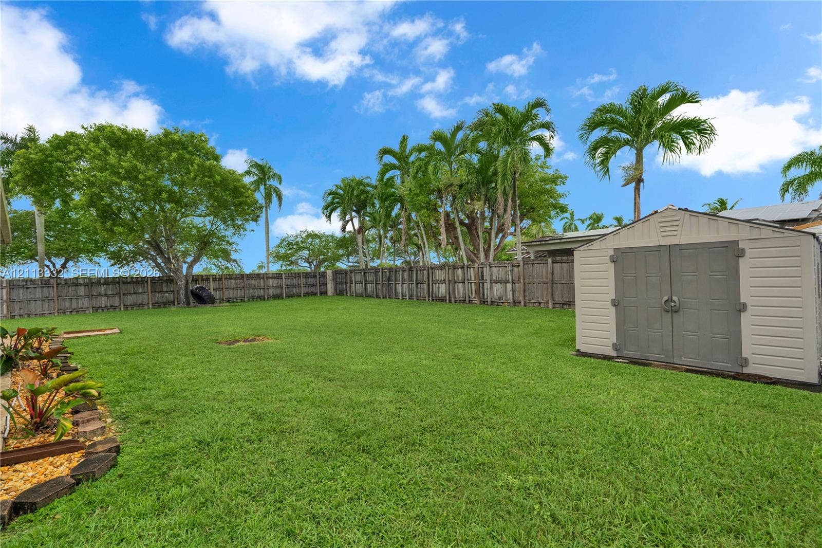 13111 SW 84th Street, Miami, FL 33183 Expansive backyard featuring a manicured lawn, full-perimeter wood fencing, mature palm trees, and an exterior storage shed