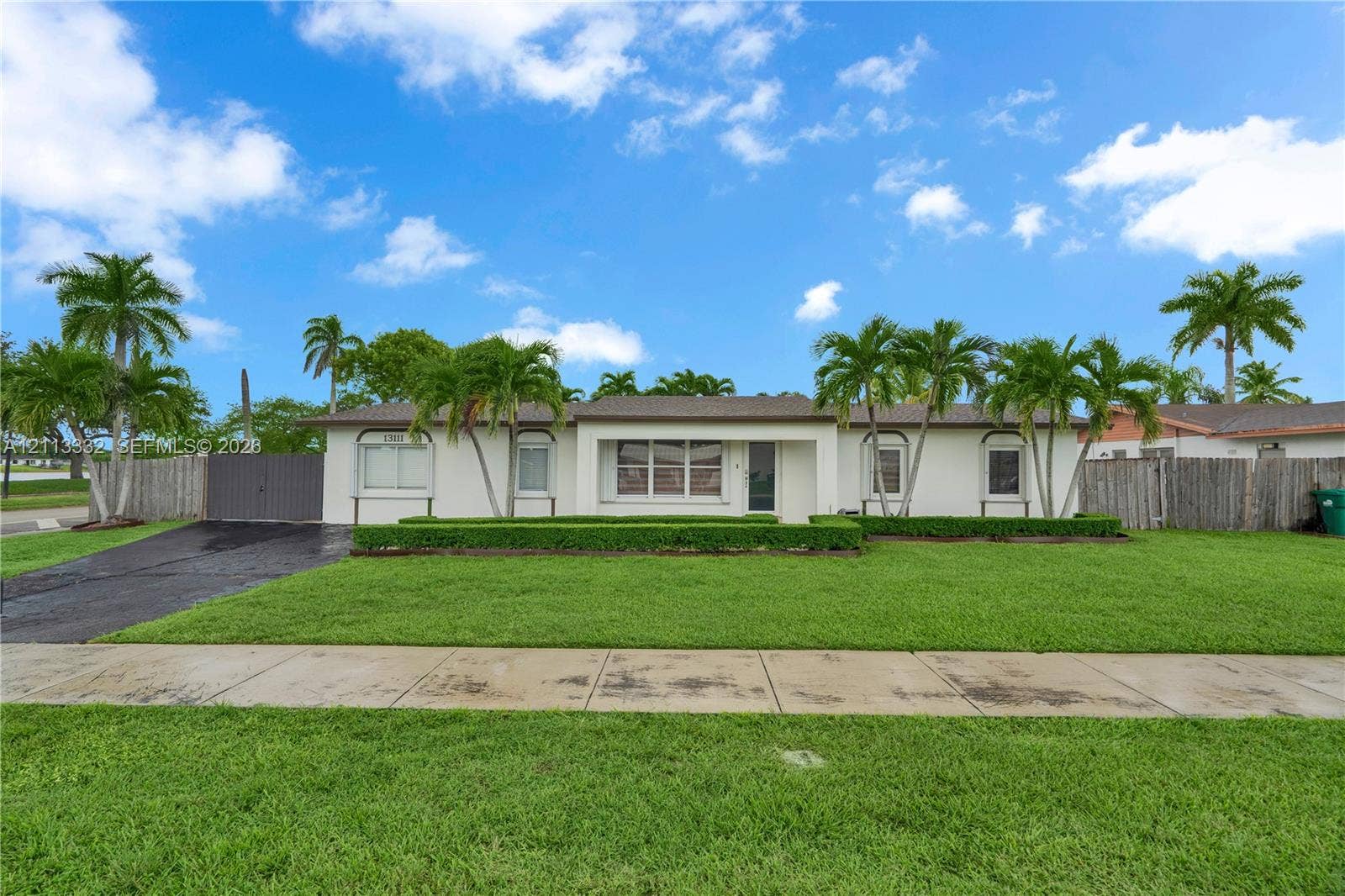 13111 SW 84th Street, Miami, FL 33183 Single-story exterior featuring light-toned stucco, a multi-pane front window, manicured shrubbery, and mature palm trees across the front lawn