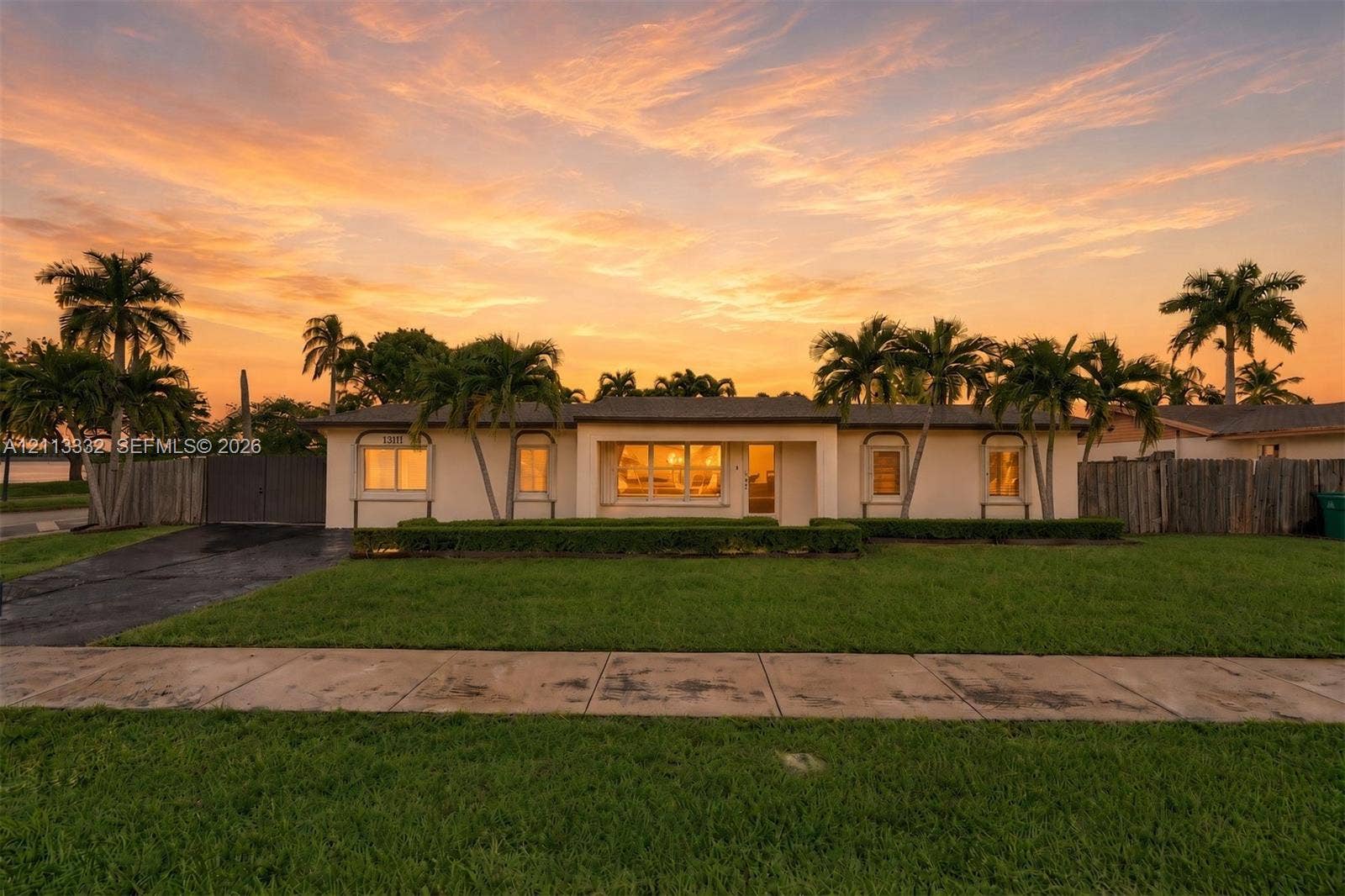 13111 SW 84th Street, Miami, FL 33183 Single-story residence featuring a stucco exterior, expansive lawn, mature palm trees, manicured hedges, and a paved driveway