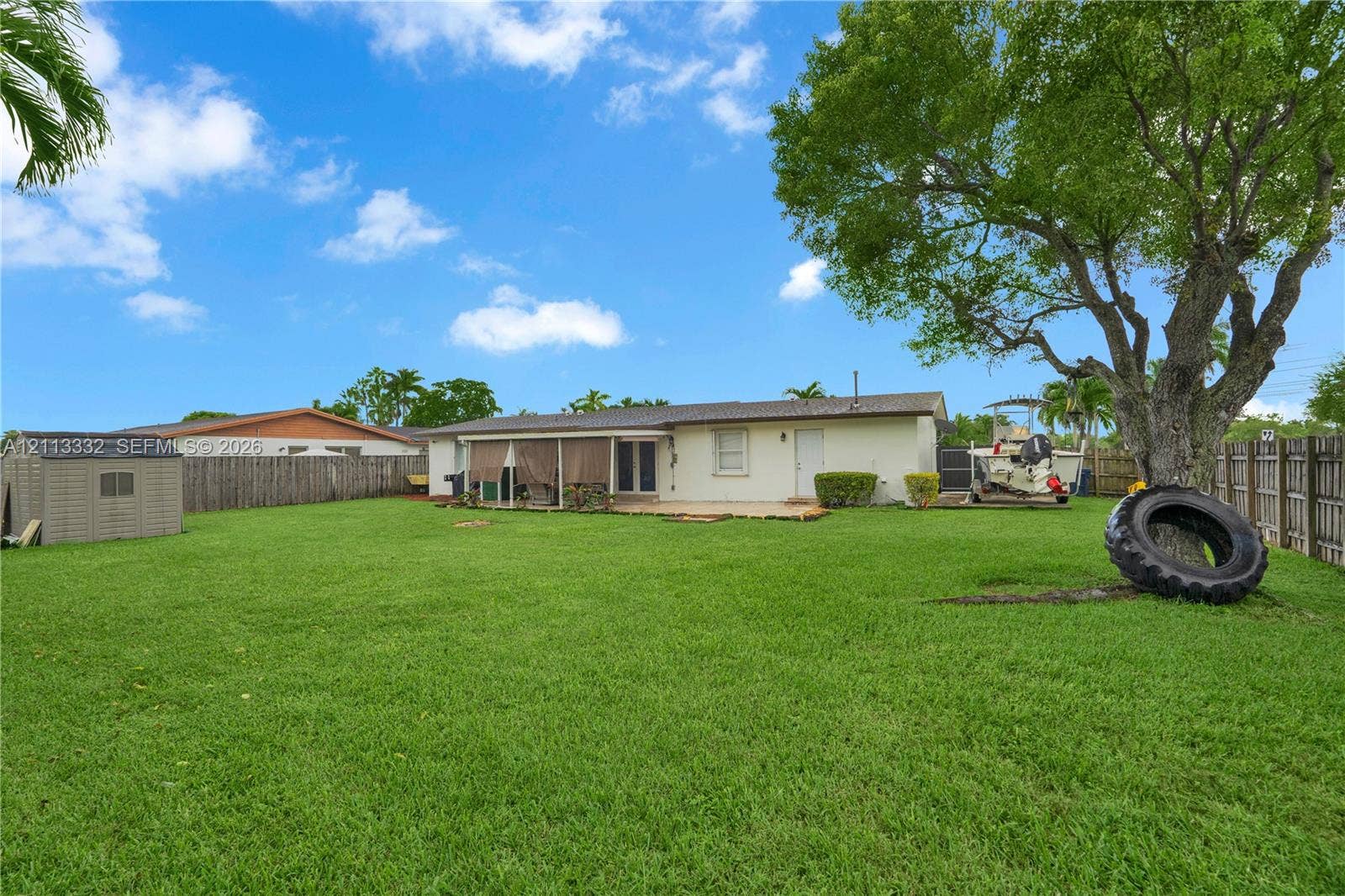 13111 SW 84th Street, Miami, FL 33183 Expansive backyard featuring a large grass lawn, perimeter wood fencing, a detached resin storage shed, and a mature shade tree