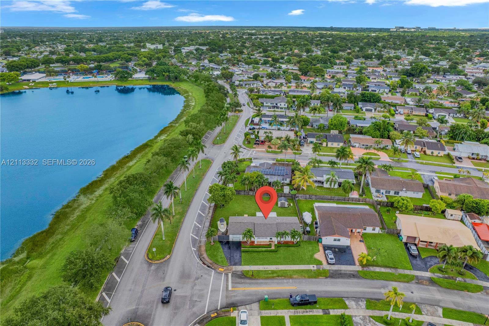 13111 SW 84th Street, Miami, FL 33183 Aerial perspective featuring a single-story residence situated on a lot bordering a large lake with expansive lawn space and mature palm trees