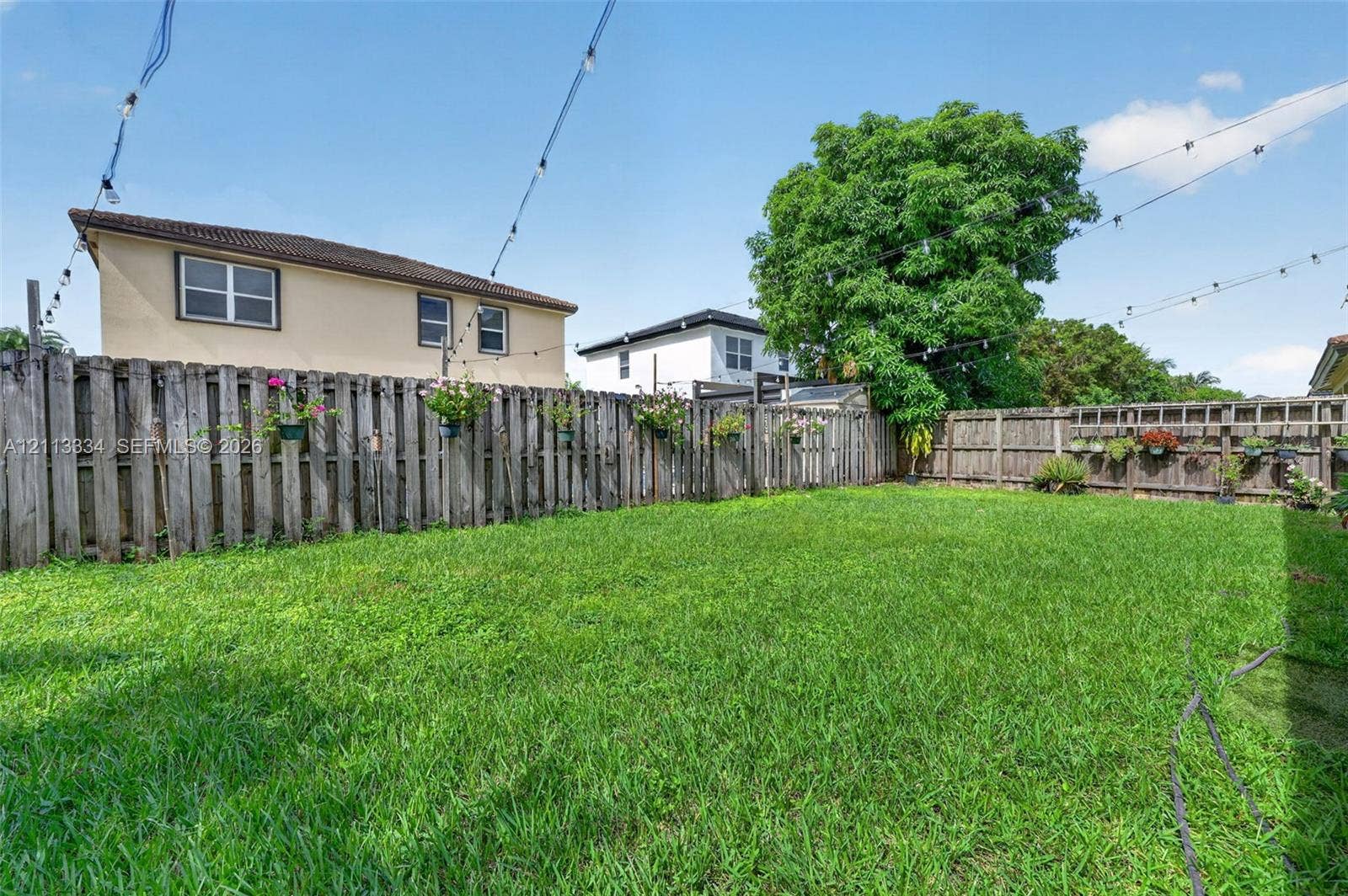 28232 SW 128th Path, Homestead, FL 33033 Expansive backyard featuring a manicured lawn, full-perimeter wood privacy fencing, and overhead string lighting