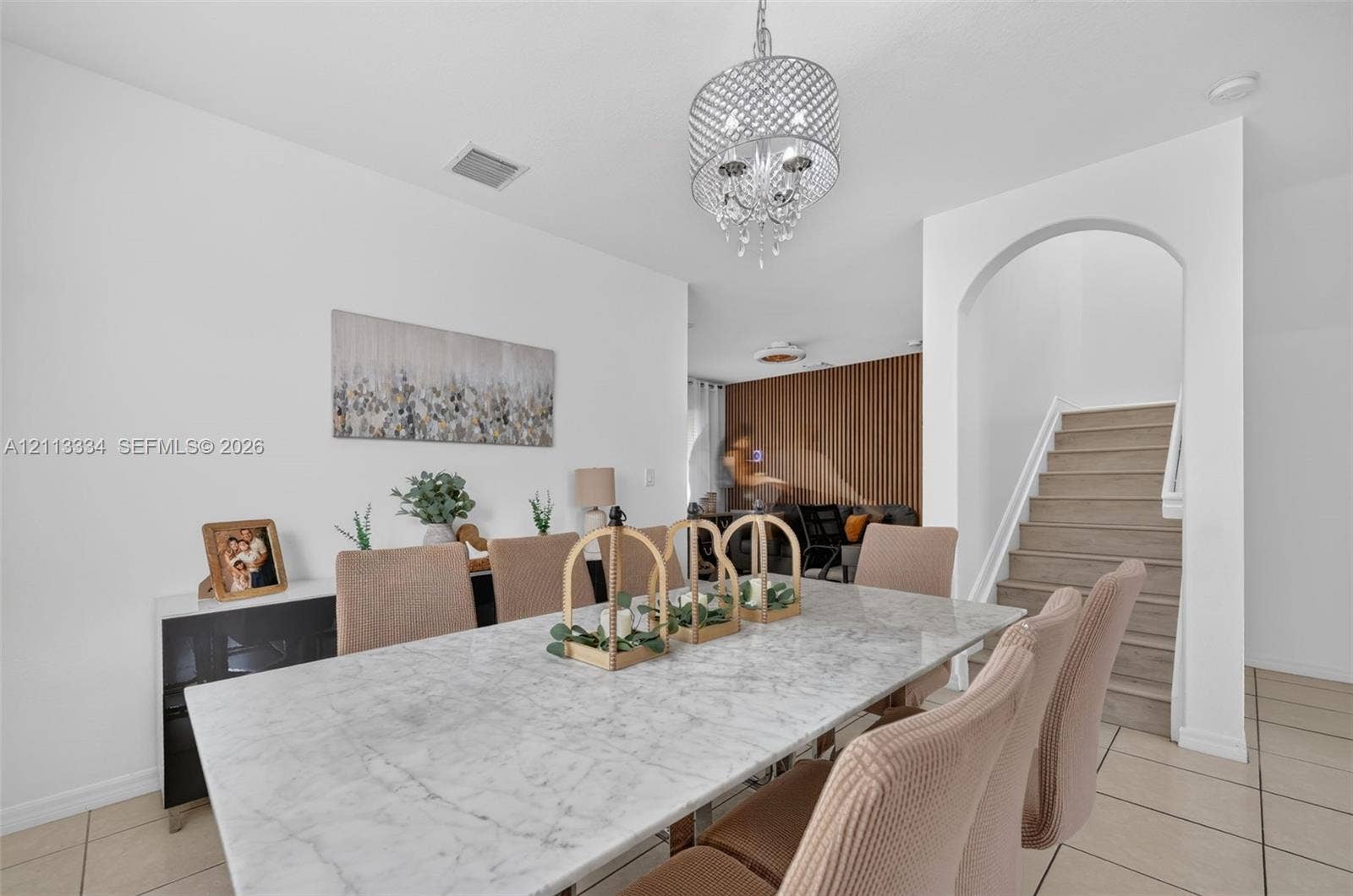28232 SW 128th Path, Homestead, FL 33033 Open-concept dining area featuring a tiered crystal chandelier, tile flooring, an arched entryway, and a vertical wood-slat accent wall
