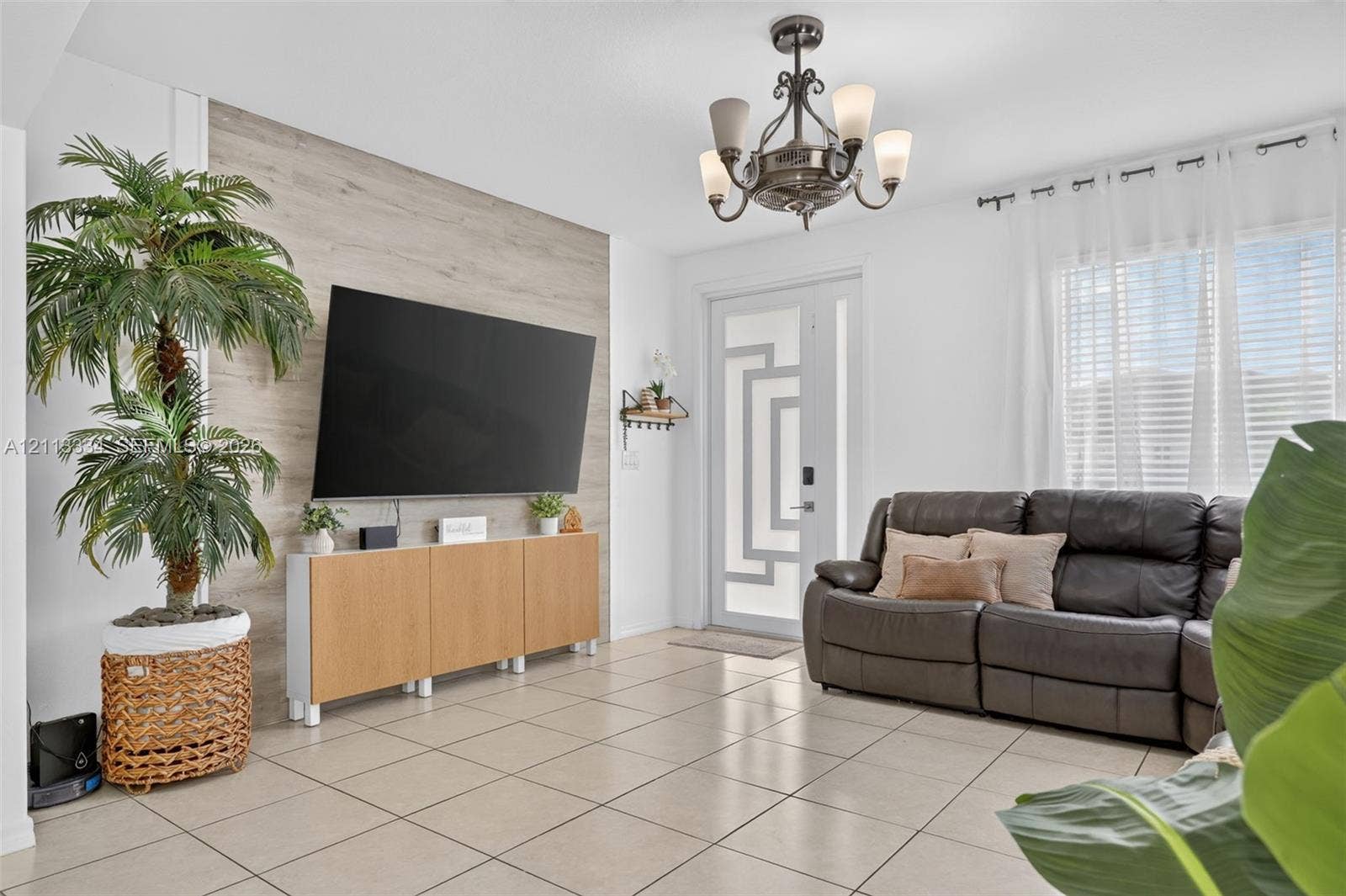 28232 SW 128th Path, Homestead, FL 33033 Living area featuring large-format tile flooring, a prominent wood-finish accent wall, a decorative five-light chandelier, and an exterior door with geometric glass paneling