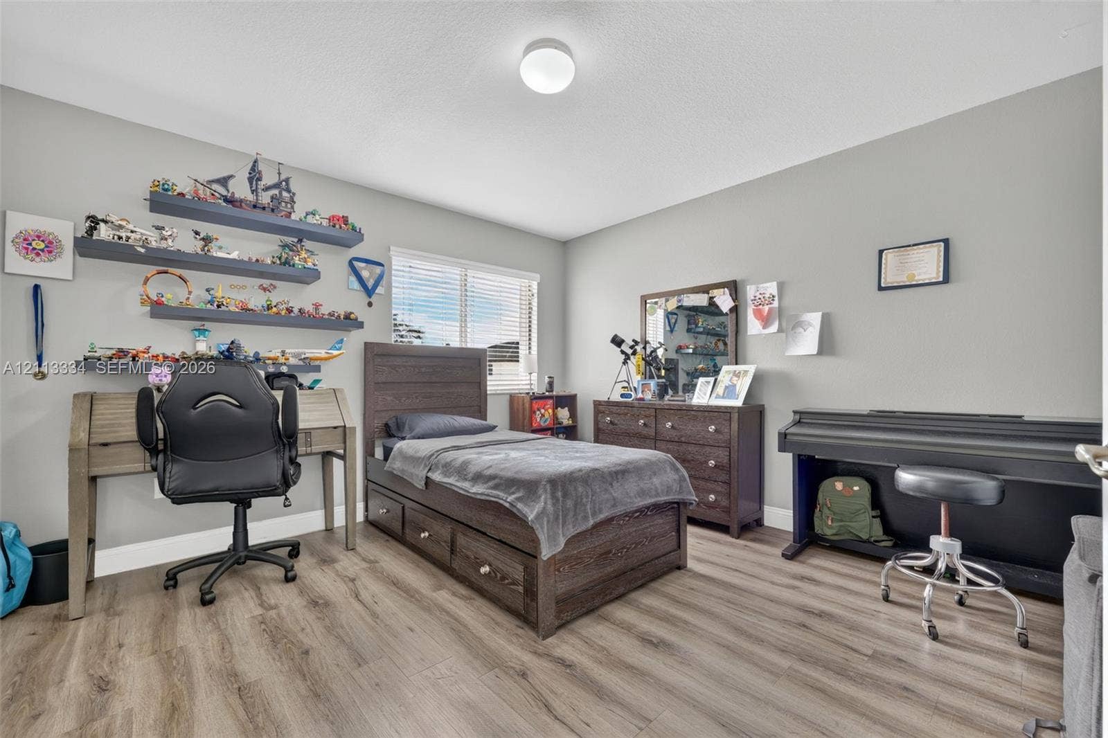 28232 SW 128th Path, Homestead, FL 33033 Neutral interior room featuring wood-finish flooring, three wall-mounted floating shelves, a single window with horizontal blinds, and a circular flush-mount ceiling light fixture