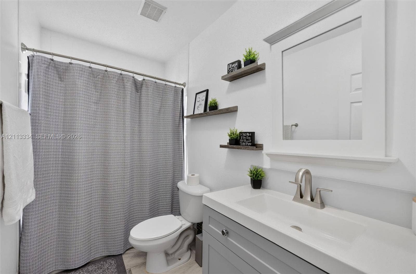 28232 SW 128th Path, Homestead, FL 33033 Bathroom featuring a vanity with a white countertop and integrated sink, brushed-nickel faucet, framed mirror, and three wall-mounted wood-finish floating shelves