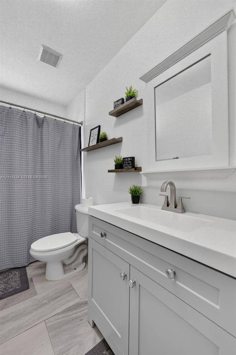 28232 SW 128th Path, Homestead, FL 33033 Bathroom featuring a vanity with a white integrated basin, brushed nickel faucet, light gray cabinetry, wall-mounted wood-finish floating shelving, and tile flooring