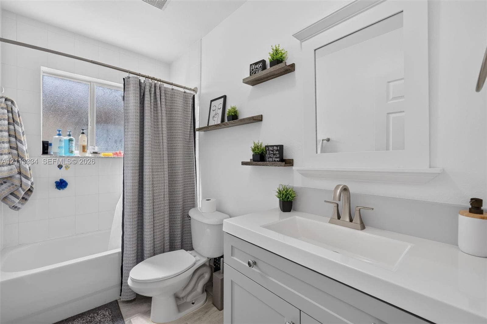 28232 SW 128th Path, Homestead, FL 33033 Bathroom featuring a gray vanity with an integrated rectangular sink, brushed nickel faucet, white-tiled shower surround, and three wood-finish wall-mounted shelves