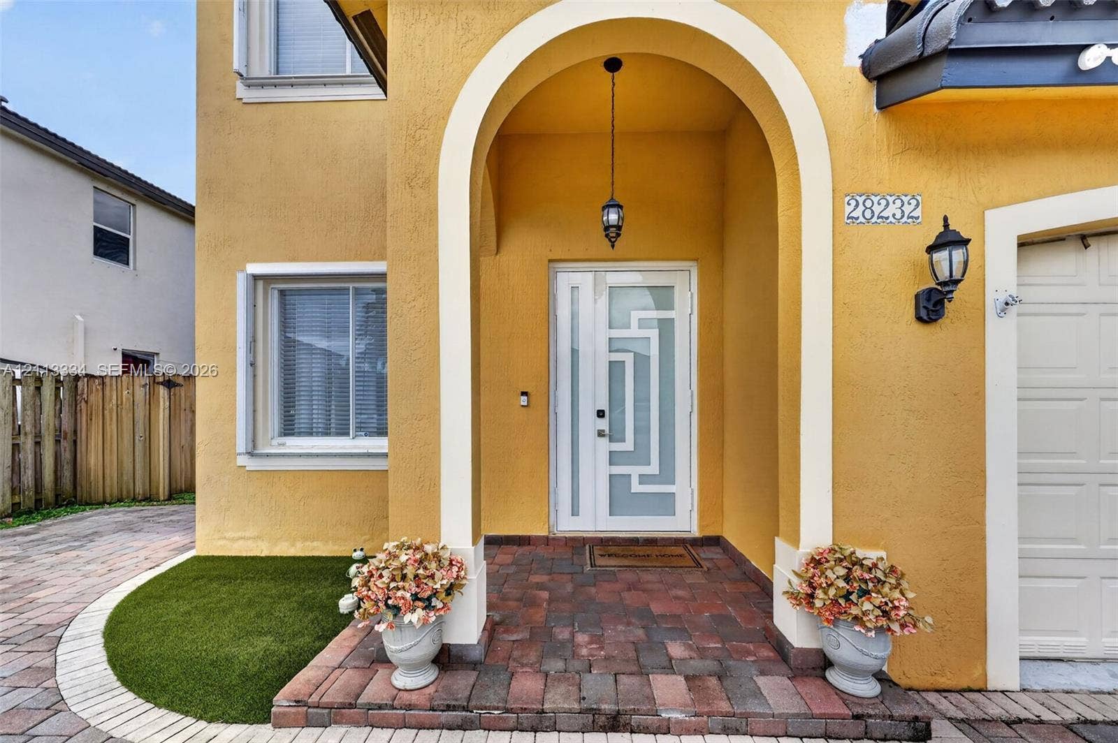 28232 SW 128th Path, Homestead, FL 33033 Stucco exterior featuring a recessed entry with an arched portico, decorative glass panel entry door, paver porch flooring, and exterior carriage lighting