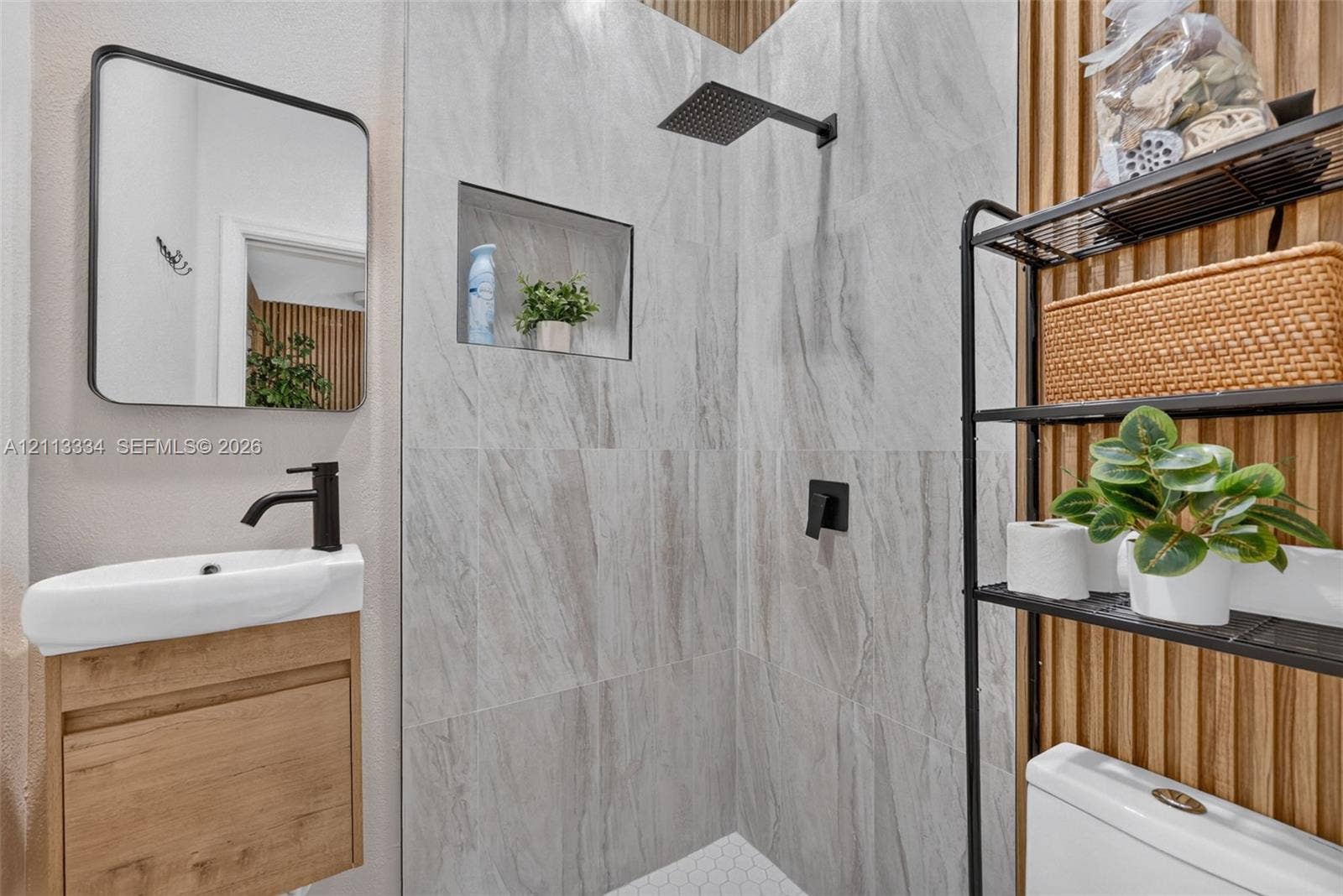 28232 SW 128th Path, Homestead, FL 33033 Wall-mounted wood-finish vanity with a rectangular sink and matte black faucet, wall-mounted mirror with black frame, walk-in shower featuring floor-to-ceiling stone-style tile, built-in shower niche, and wood-slat accent wall