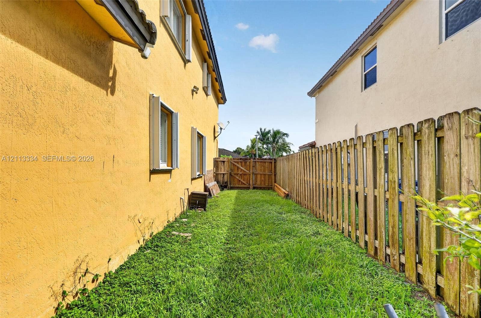 28232 SW 128th Path, Homestead, FL 33033 Exterior side yard featuring stucco siding, grass lawn, and a wooden privacy fence with a gated entry